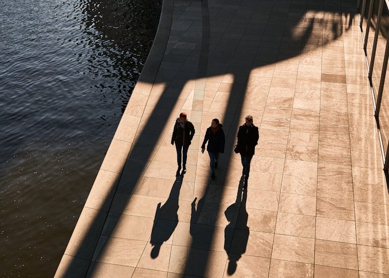 Meine Vision Drei Personen gehen entlang einer Uferpromenade, ihre Schatten sind zu sehen.