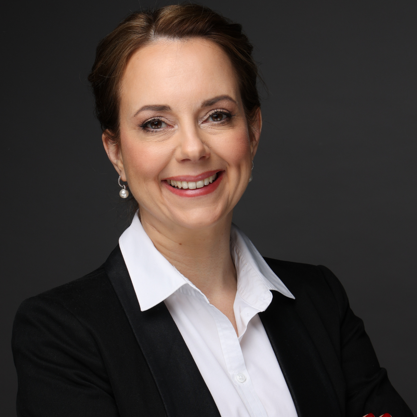 Kathrin Hölzel Frau mit einem freundlichen Lächeln, trägt einen schwarzen Blazer und ein weißes Hemd.